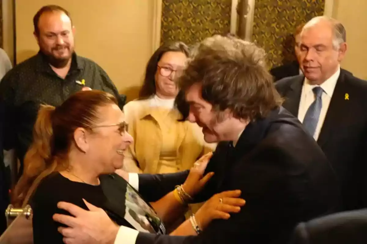 Un hombre y una mujer se saludan sonrientes en un ambiente formal mientras otras personas observan en el fondo Un hombre y una mujer se saludan sonrientes en un ambiente formal mientras otras personas observan en el fondo