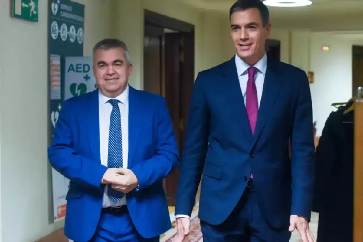 Two men in suits walk together down a brightly lit hallway in an institutional building. Two men in suits walk together down a brightly lit hallway in an institutional building.