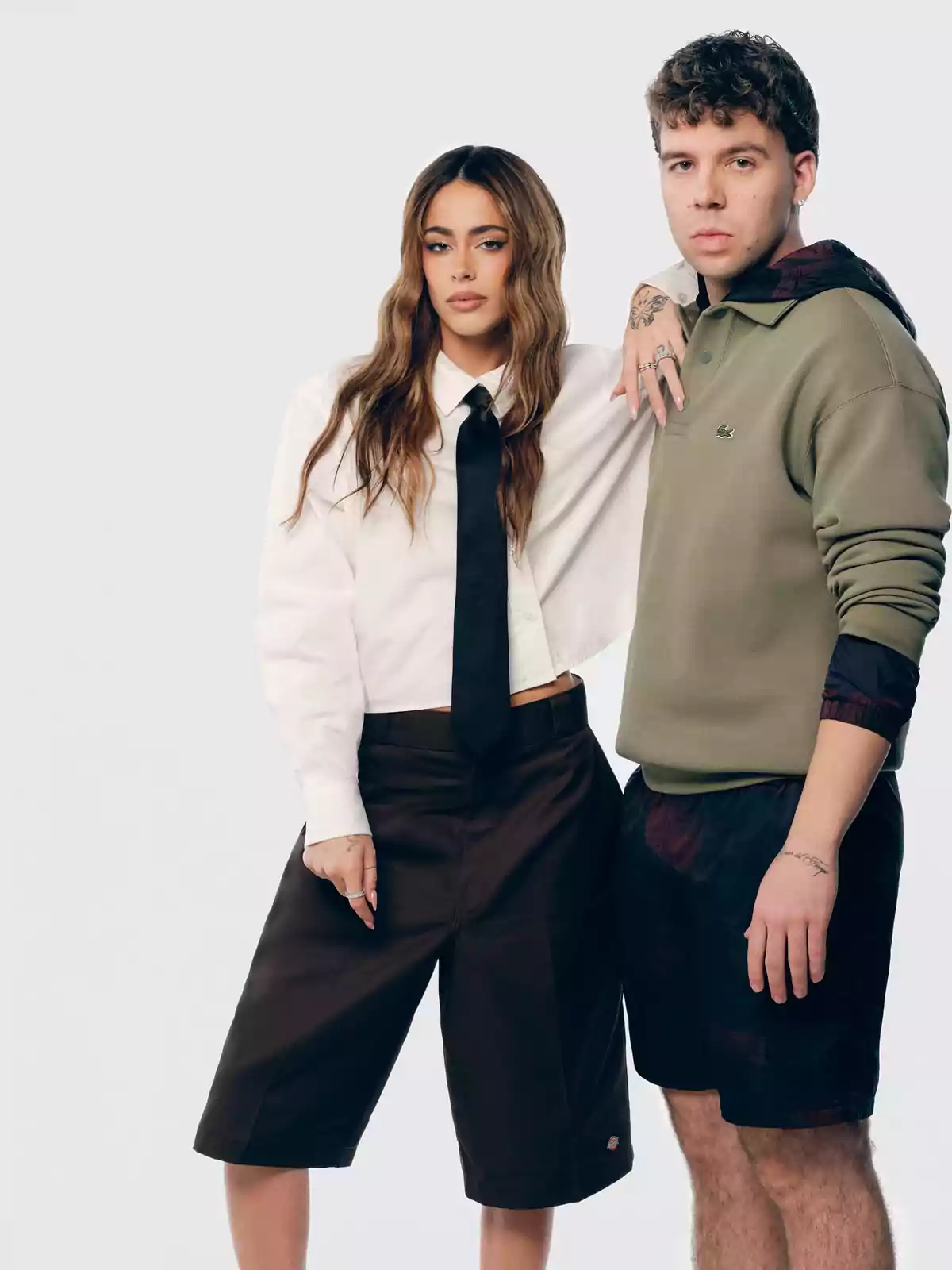 Dos personas posando juntas, una mujer con camisa blanca y corbata negra y un hombre con sudadera verde. Dos personas posando juntas, una mujer con camisa blanca y corbata negra y un hombre con sudadera verde.