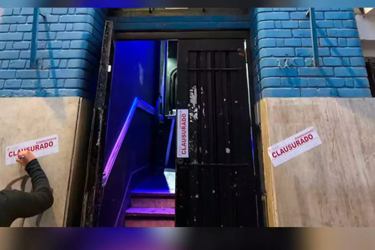 Puerta de entrada con letreros de clausurado y una persona colocando uno de ellos en la pared Puerta de entrada con letreros de clausurado y una persona colocando uno de ellos en la pared