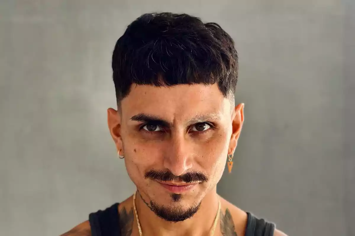 Un hombre con cabello corto y barba, usando aretes y una camiseta sin mangas, mirando directamente a la cámara con una expresión seria.