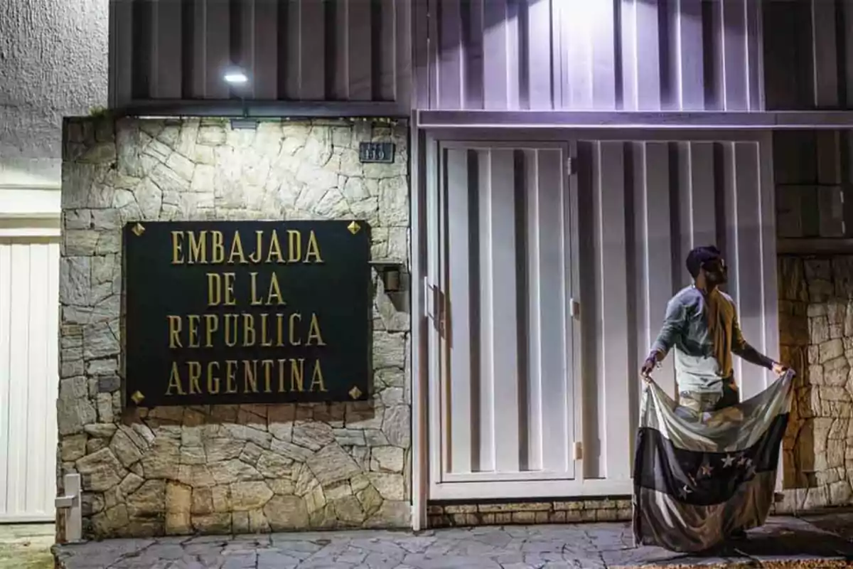 Un hombre sostiene una bandera frente a la Embajada de la República Argentina.