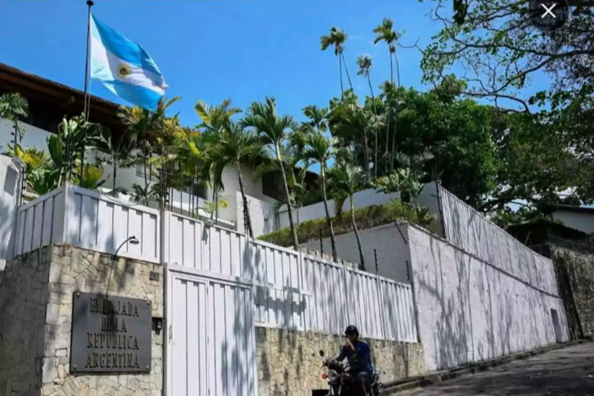 Edificio de la embajada de Argentina con una bandera ondeando y un motociclista pasando por la calle.