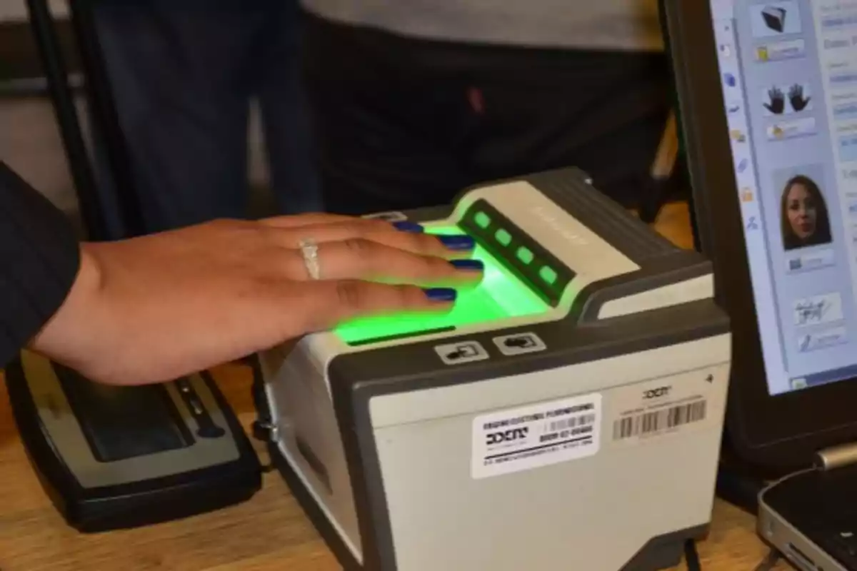 Una persona coloca su mano sobre un escáner biométrico mientras un monitor muestra información relacionada.