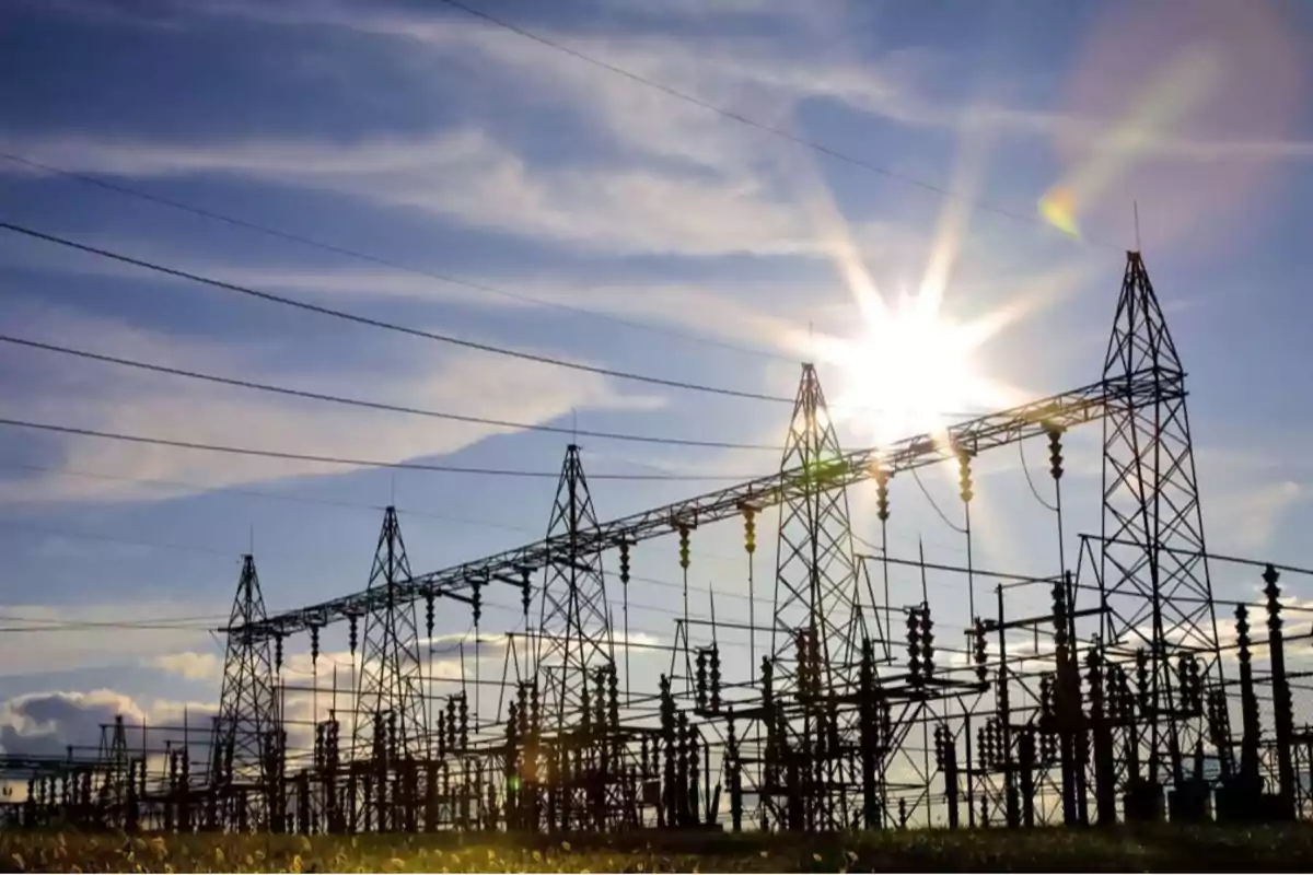 Torres y cables de una subestación eléctrica al atardecer con el sol brillando detrás de la estructura Torres y cables de una subestación eléctrica al atardecer con el sol brillando detrás de la estructura