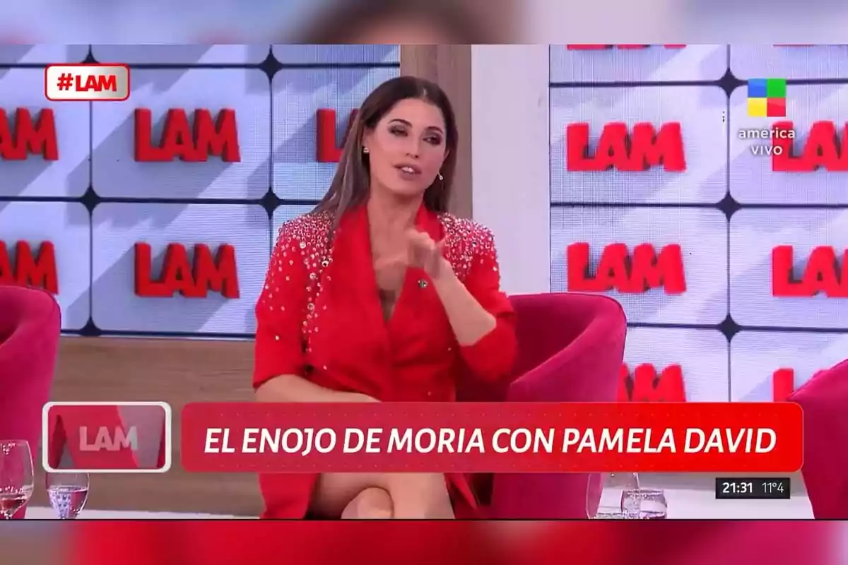 Una mujer vestida de rojo está sentada en un set de televisión con el logo de Una mujer vestida de rojo está sentada en un set de televisión con el logo de