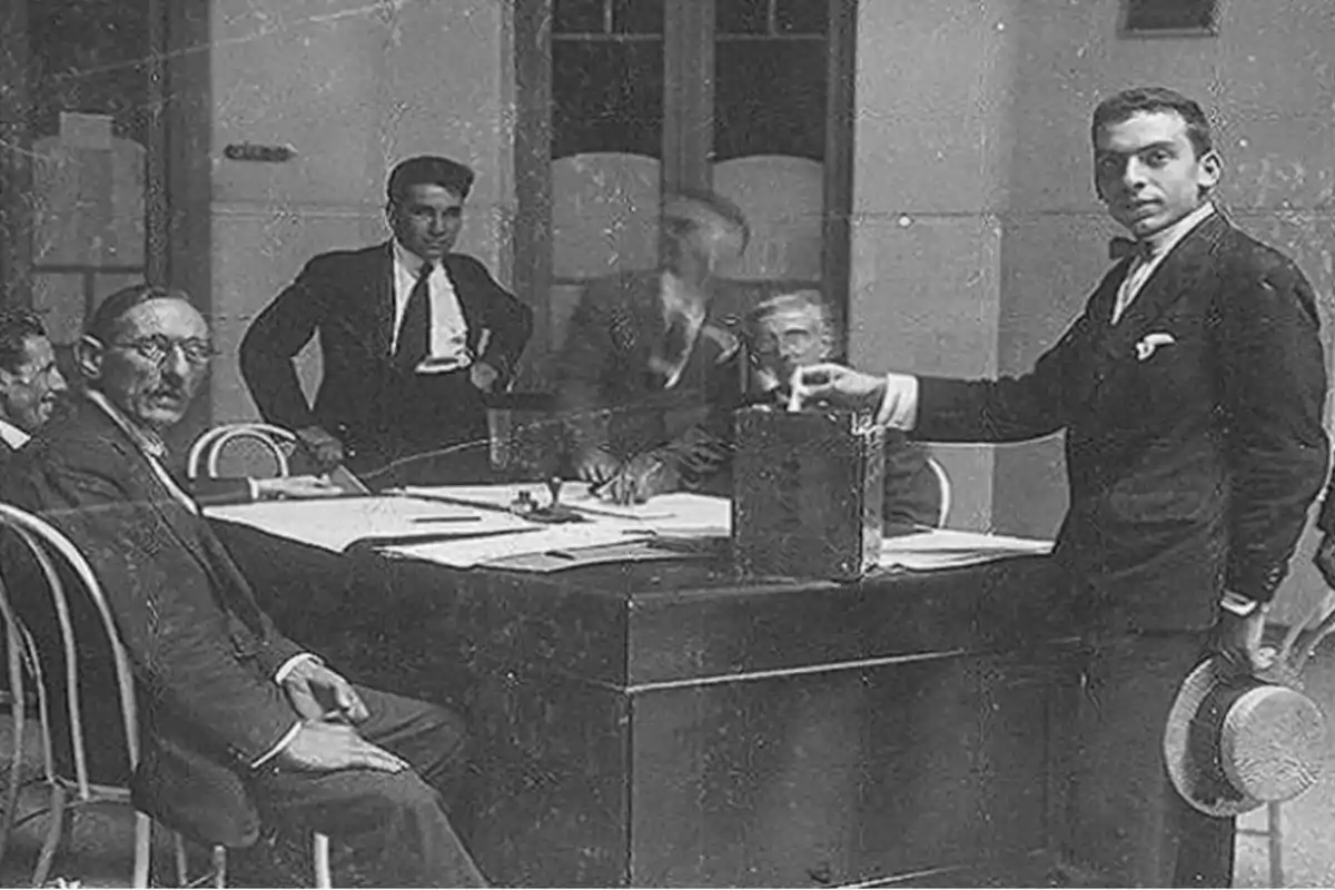 A group of men in suits is gathered around a table, one of them is placing a paper in a ballot box. A group of men in suits is gathered around a table, one of them is placing a paper in a ballot box.