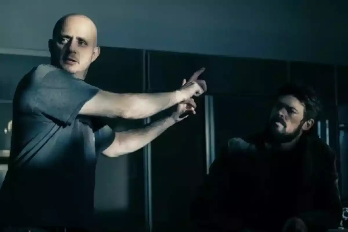 Two men in a dark room, one of them is pointing at something while the other watches intently. Two men in a dark room, one of them is pointing at something while the other watches intently.