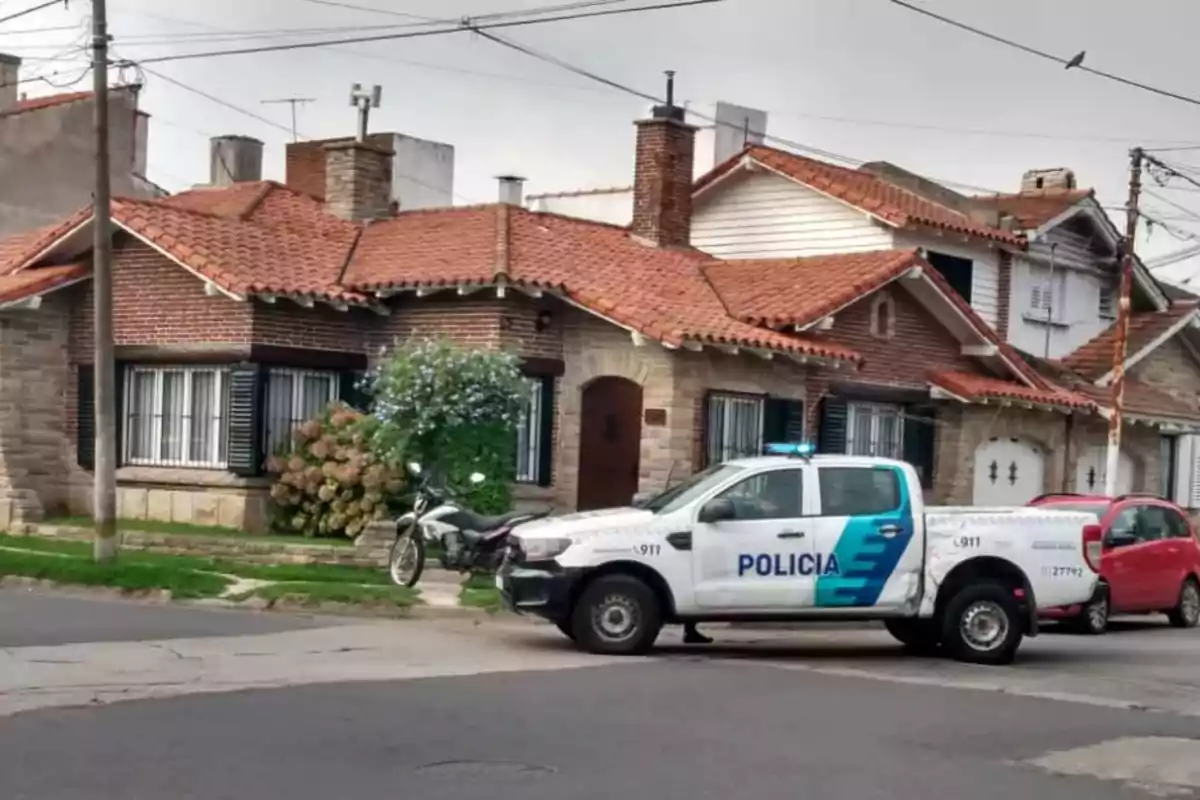 Una camioneta de la policía estacionada frente a una casa de ladrillos con techo de tejas rojas y una motocicleta al lado.