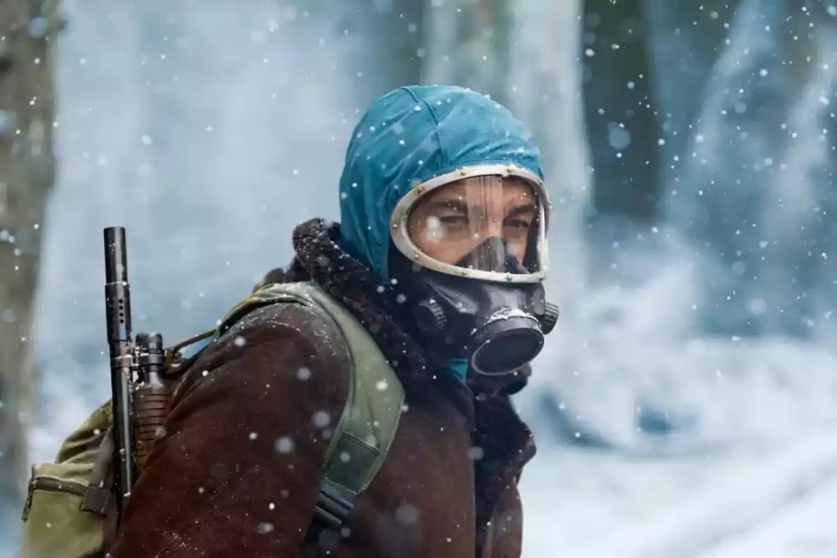 Person with a gas mask and blue hood in a snowy environment.