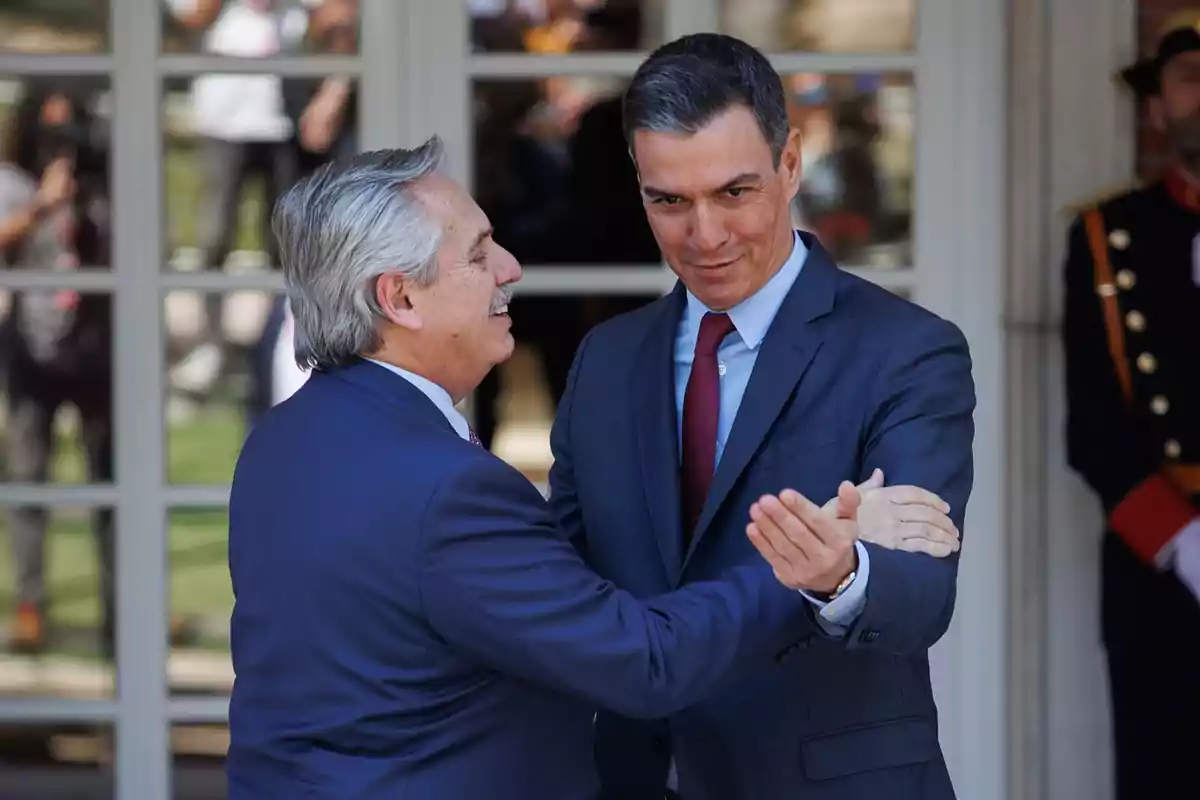 Dos hombres de traje se saludan cordialmente frente a una puerta de vidrio.