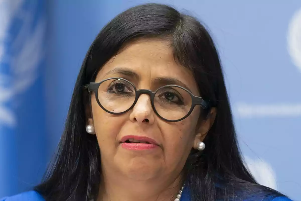 Mujer con gafas y cabello oscuro hablando frente a un fondo azul con el logo de la ONU.