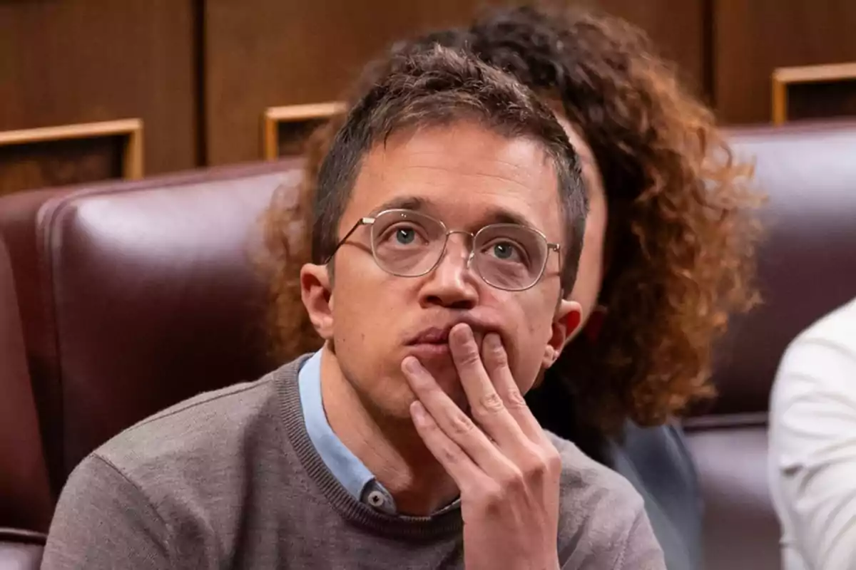 Un hombre con gafas y su mano en la barbilla parece pensativo mientras está sentado en una silla de cuero.