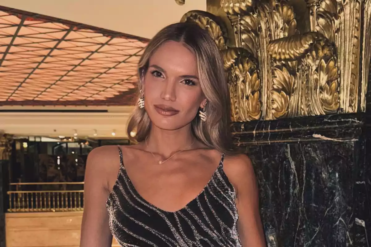 Woman in an elegant dress posing in an interior with golden decor and a geometric ceiling.