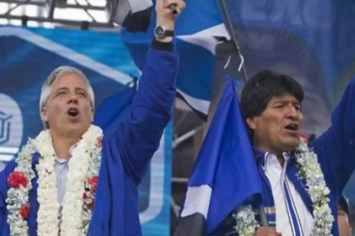Two men with flower garlands and blue flags raise their arms at a public event. Two men with flower garlands and blue flags raise their arms at a public event.