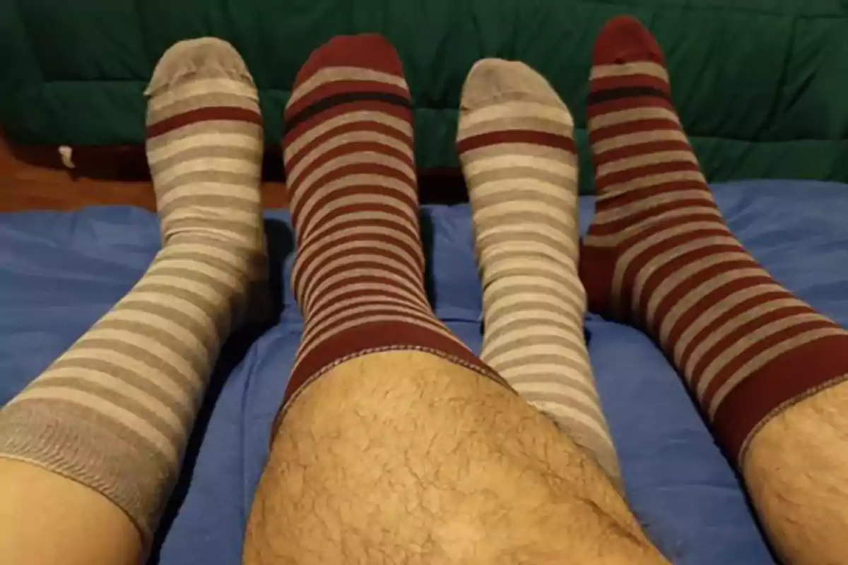 Two pairs of feet with striped socks in different colors rest on a blue surface. Two pairs of feet with striped socks in different colors rest on a blue surface.