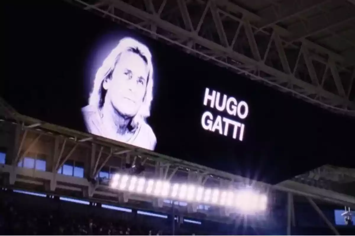 Giant screen in a stadium showing a black and white image of a person with the name Hugo Gatti.