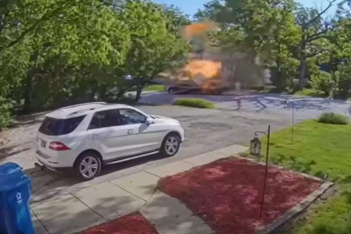 Explosión de un vehículo en una calle residencial con un auto blanco estacionado en primer plano y árboles alrededor Explosión de un vehículo en una calle residencial con un auto blanco estacionado en primer plano y árboles alrededor
