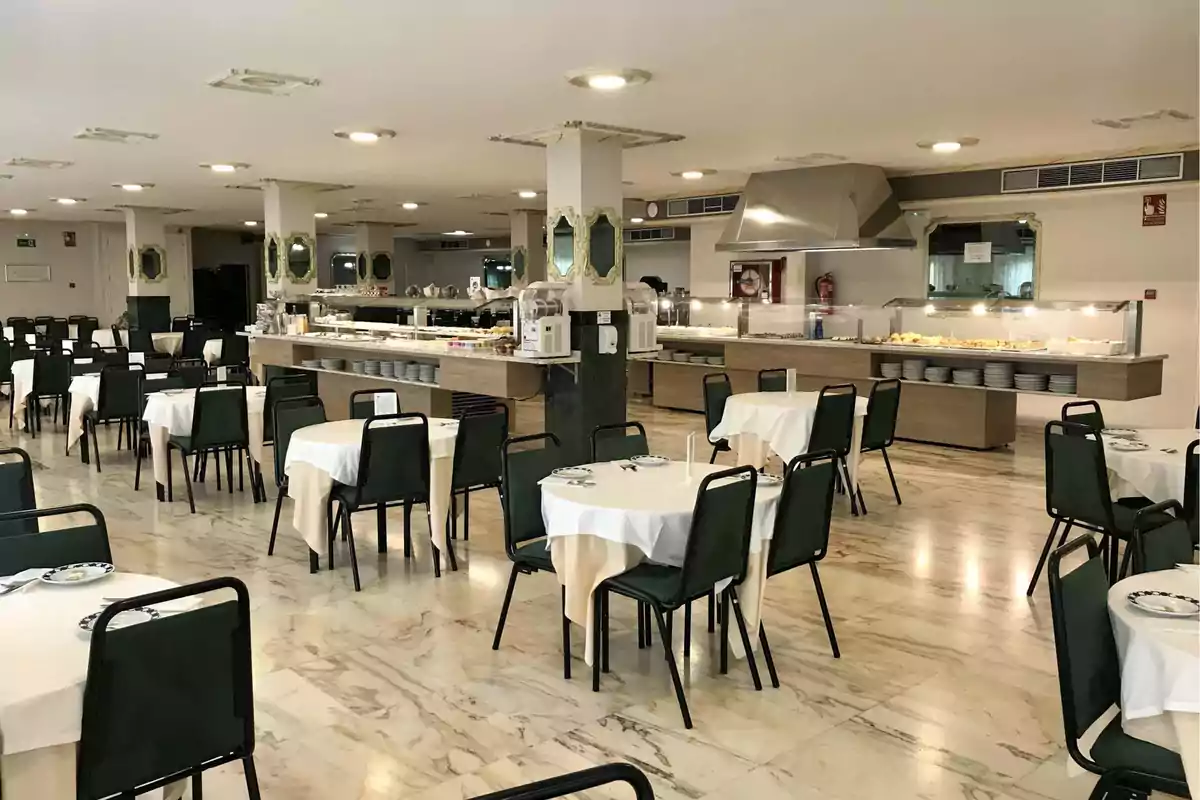 Un comedor de restaurante con mesas y sillas dispuestas ordenadamente, y una estación de buffet al fondo.