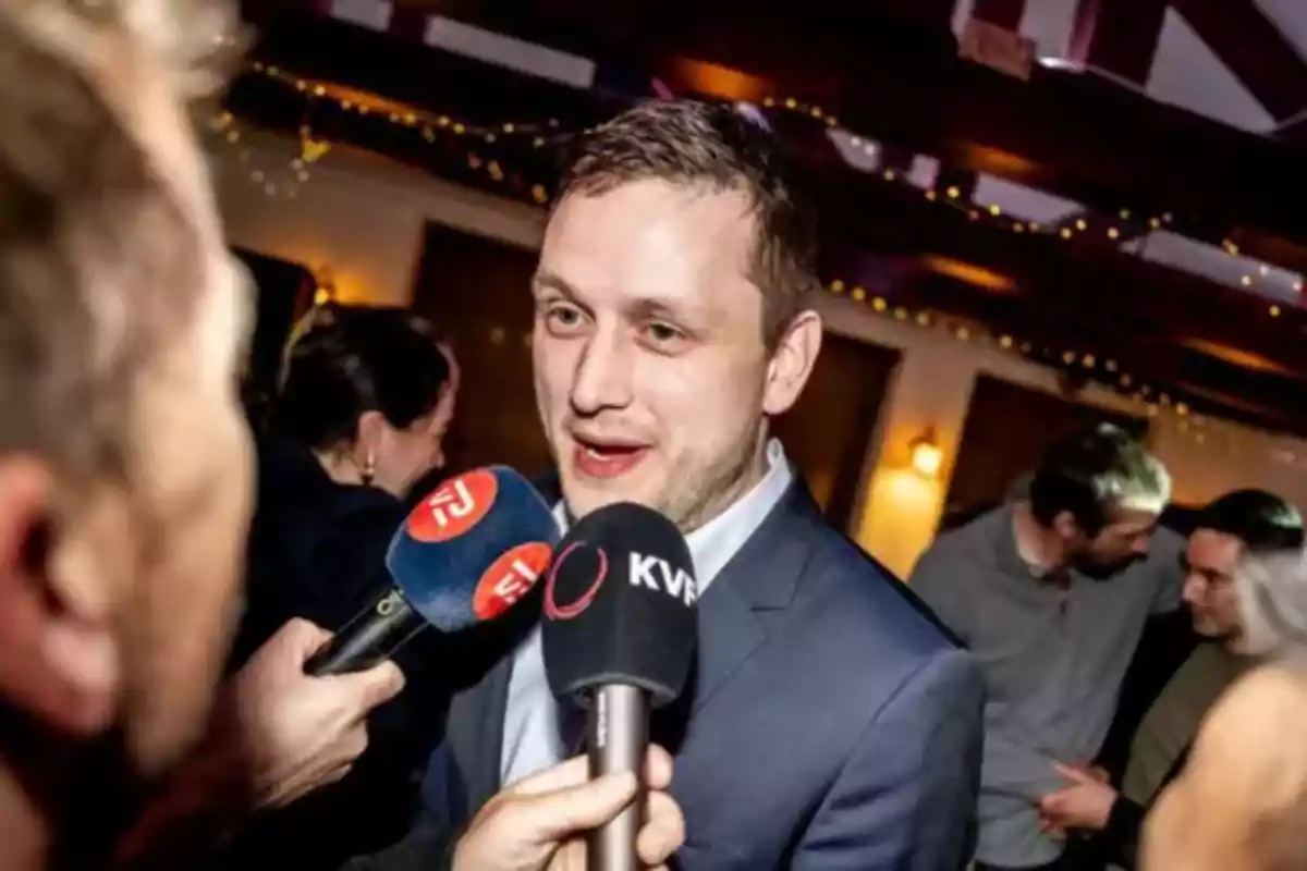 A man in a suit is being interviewed by several journalists at a social event.