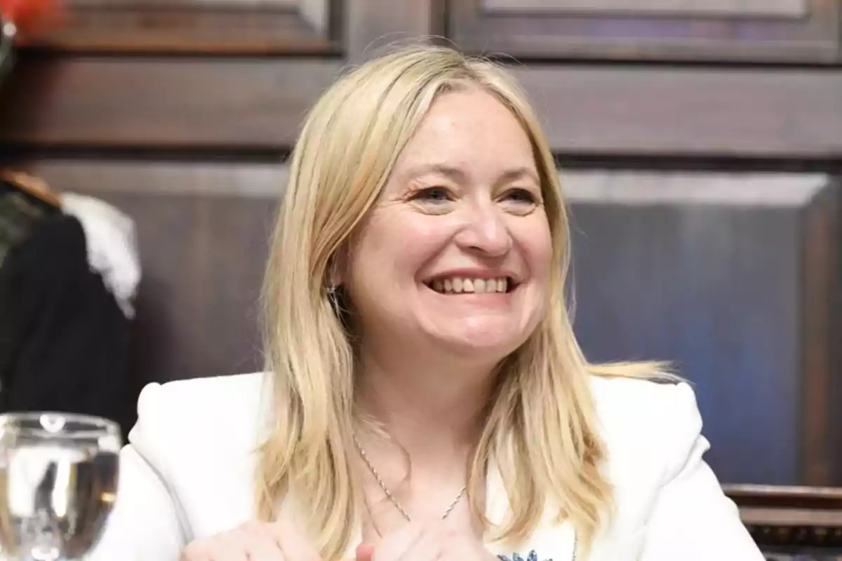 A smiling blonde woman in a white jacket in an indoor setting. A smiling blonde woman in a white jacket in an indoor setting.