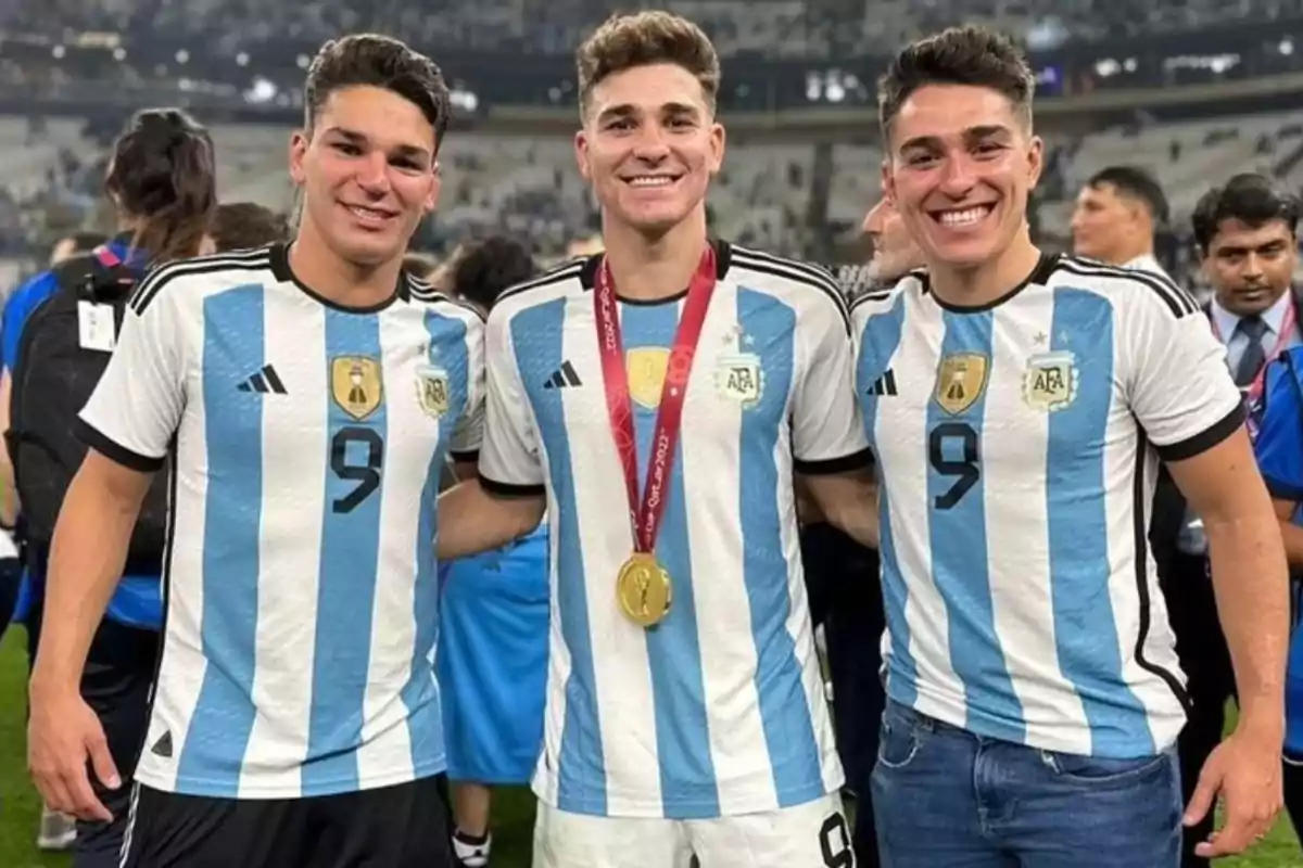 Tres personas con camisetas de la selección argentina de fútbol posan sonriendo en un estadio.