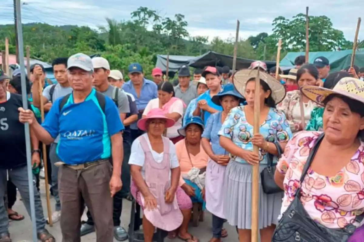 Un grupo de personas, algunas con sombreros y palos, se encuentra reunido al aire libre en un entorno natural.