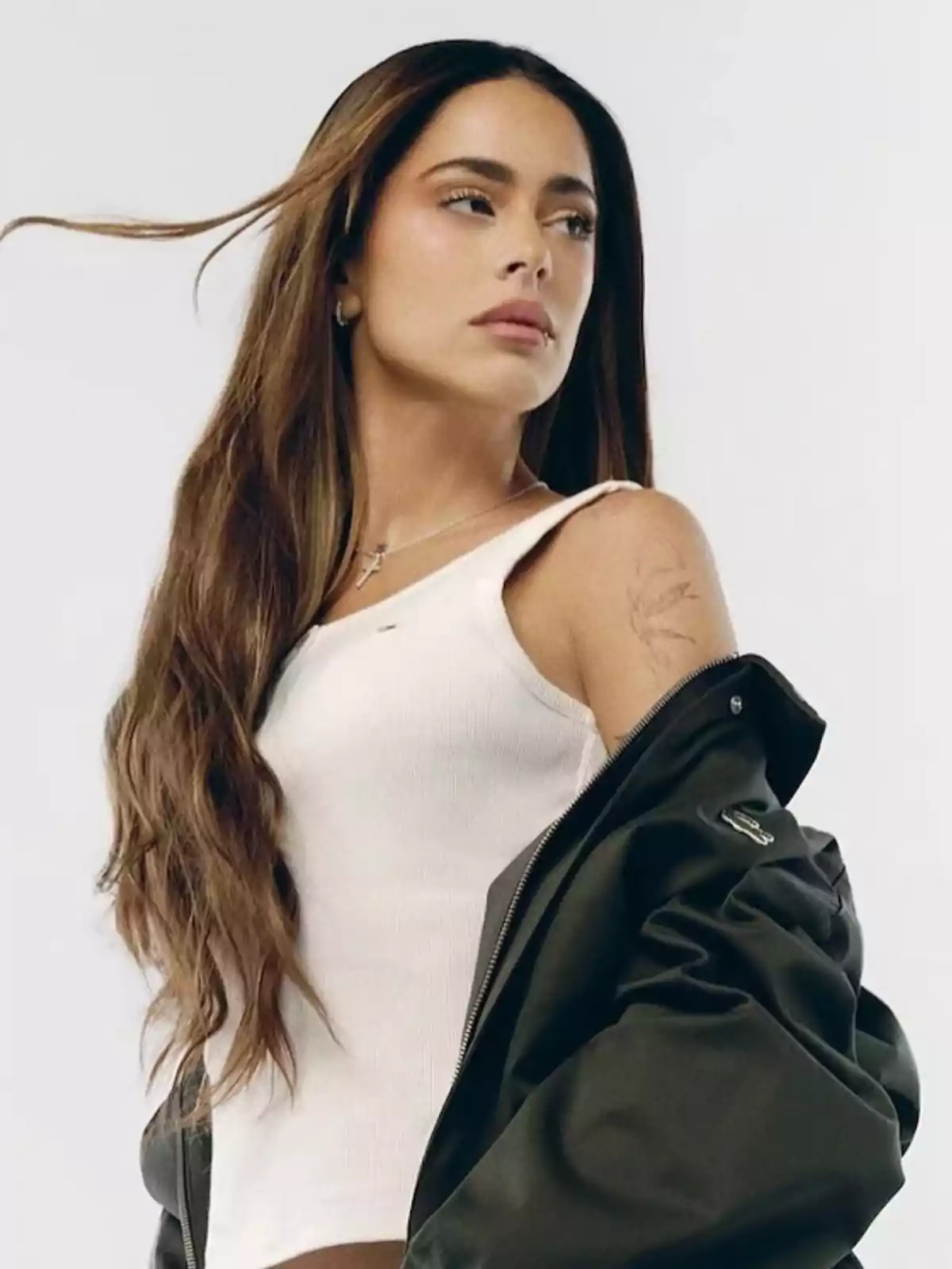 Una persona con cabello largo y suelto, vistiendo una camiseta blanca y una chaqueta oscura, mirando hacia un lado. Una persona con cabello largo y suelto, vistiendo una camiseta blanca y una chaqueta oscura, mirando hacia un lado.