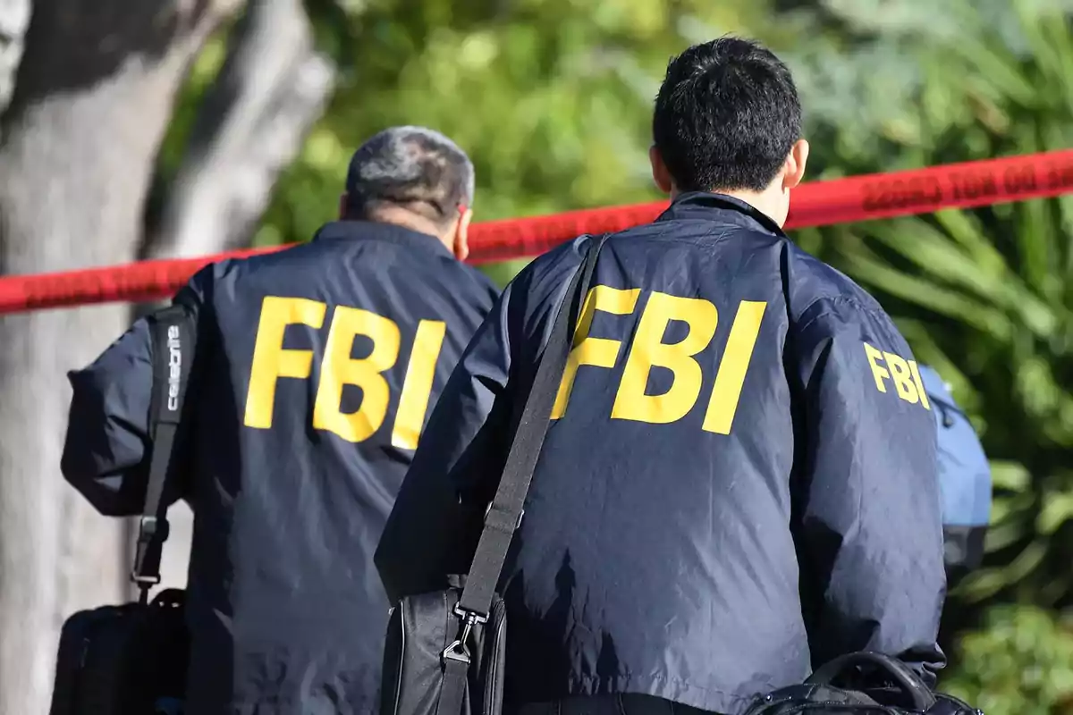 Dos agentes del FBI con chaquetas azules y letras amarillas caminan hacia una escena delimitada por cinta roja.