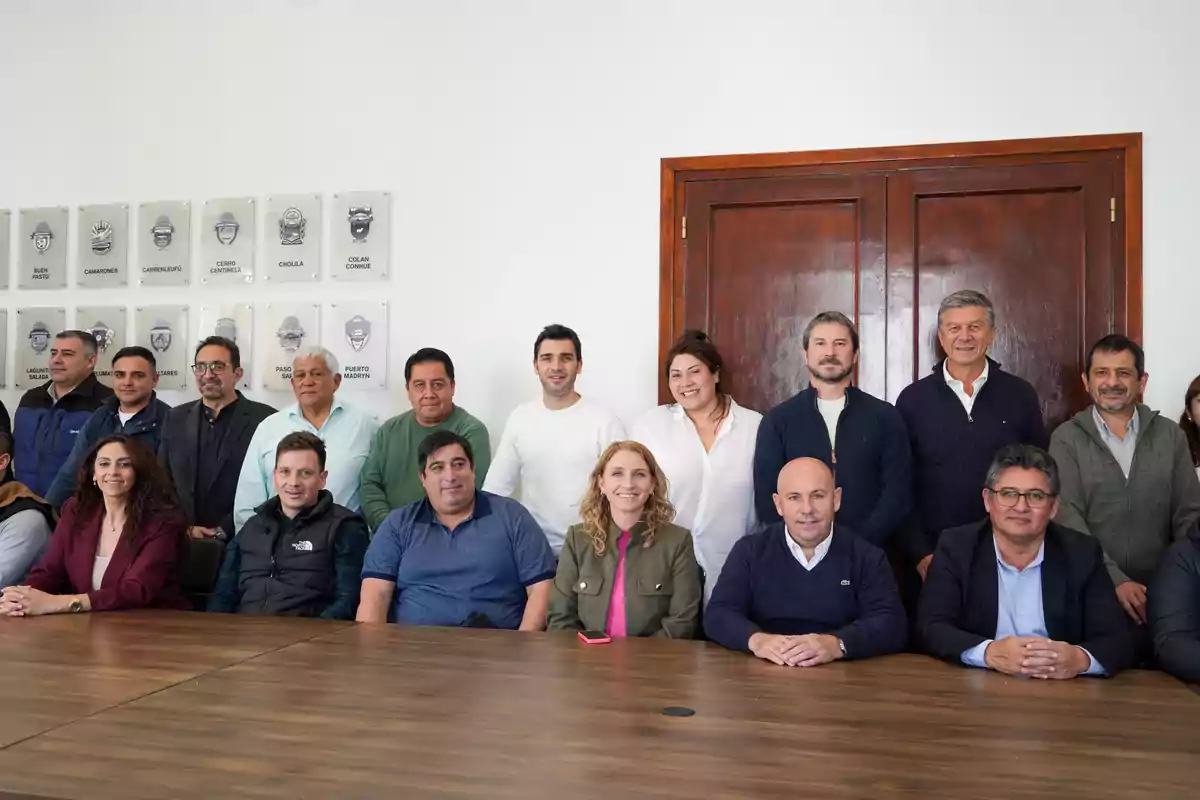 Un grupo de personas posando juntas en una sala de reuniones con una mesa de madera y una puerta de madera al fondo.