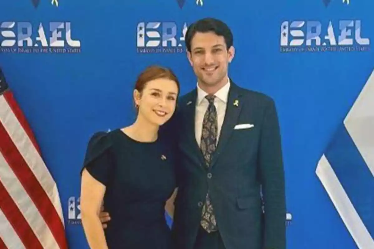 A smiling couple poses in front of a blue background with the logo of the Israeli embassy and a U.S. flag on the left. A smiling couple poses in front of a blue background with the logo of the Israeli embassy and a U.S. flag on the left.