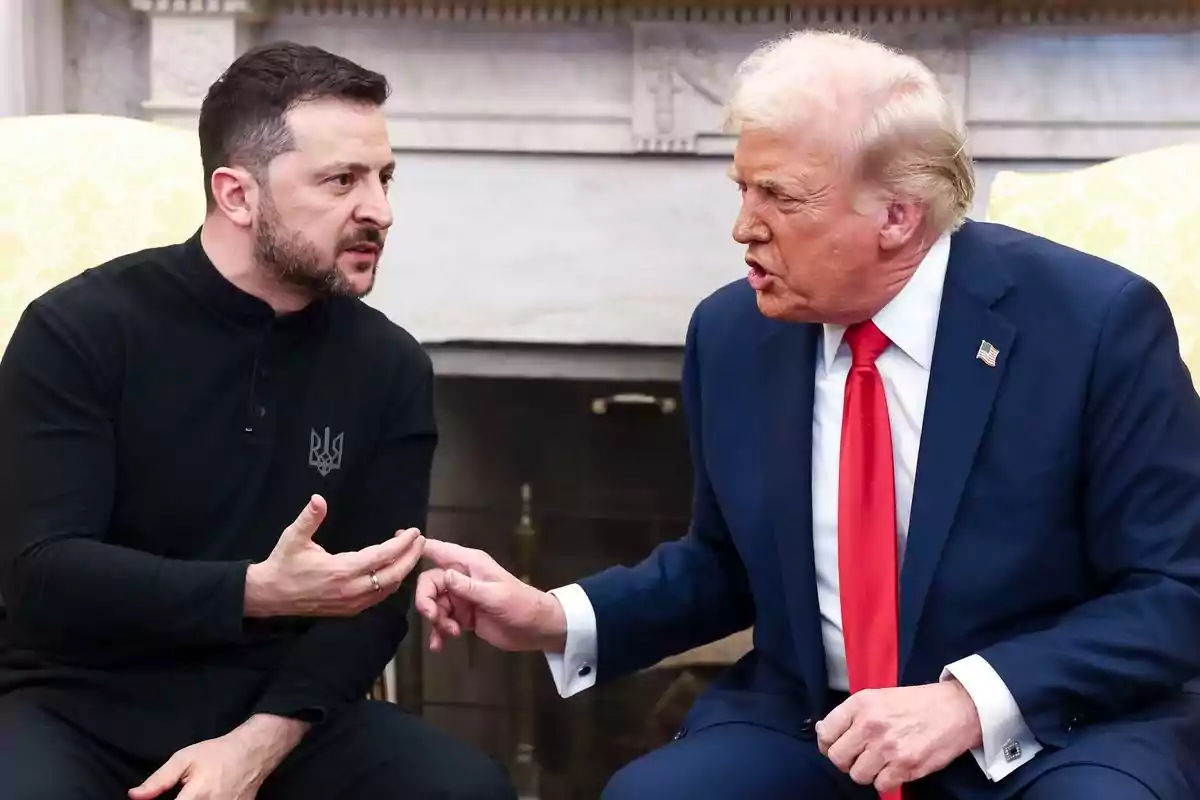 Two men sitting face to face in a serious conversation, one in a blue suit and red tie, the other in a black jersey.