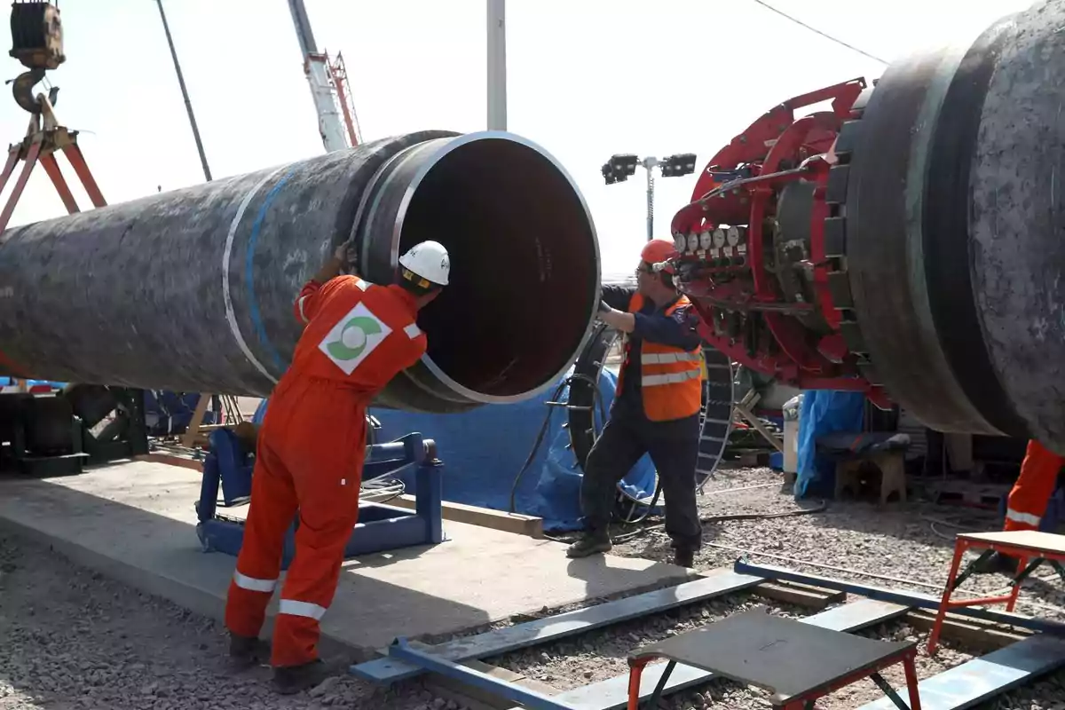 Trabajadores con cascos y uniformes de seguridad manipulan grandes tuberías en un sitio de construcción al aire libre. Trabajadores con cascos y uniformes de seguridad manipulan grandes tuberías en un sitio de construcción al aire libre.
