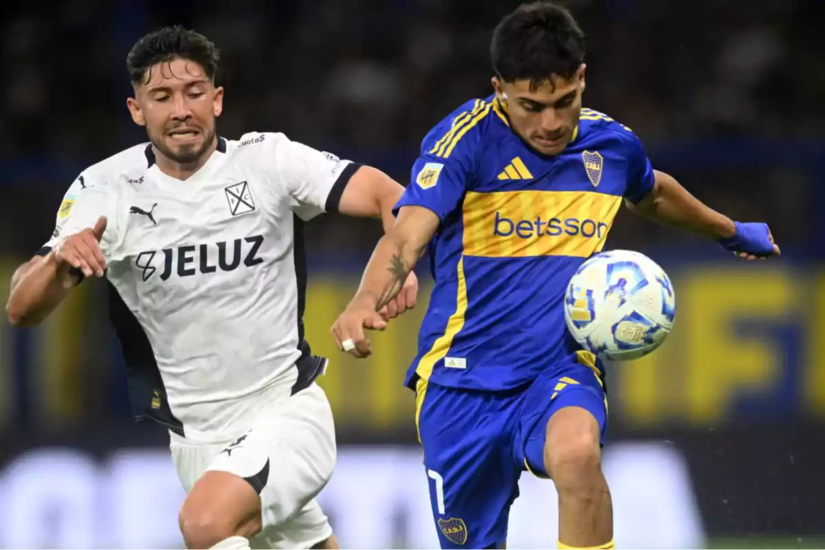 Dos jugadores de fútbol compiten por el balón en un partido, uno viste uniforme blanco y el otro azul y amarillo. Dos jugadores de fútbol compiten por el balón en un partido, uno viste uniforme blanco y el otro azul y amarillo.