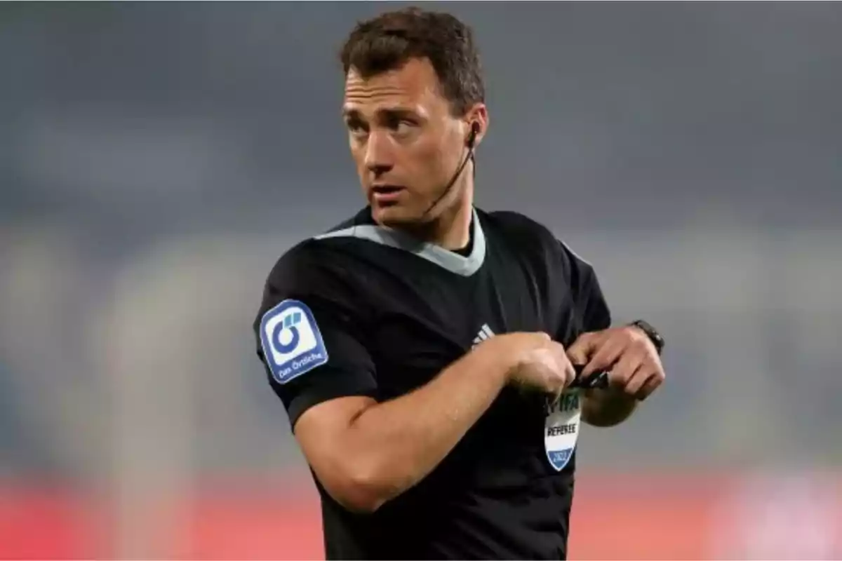 Soccer referee in a black uniform with an earpiece on the field.