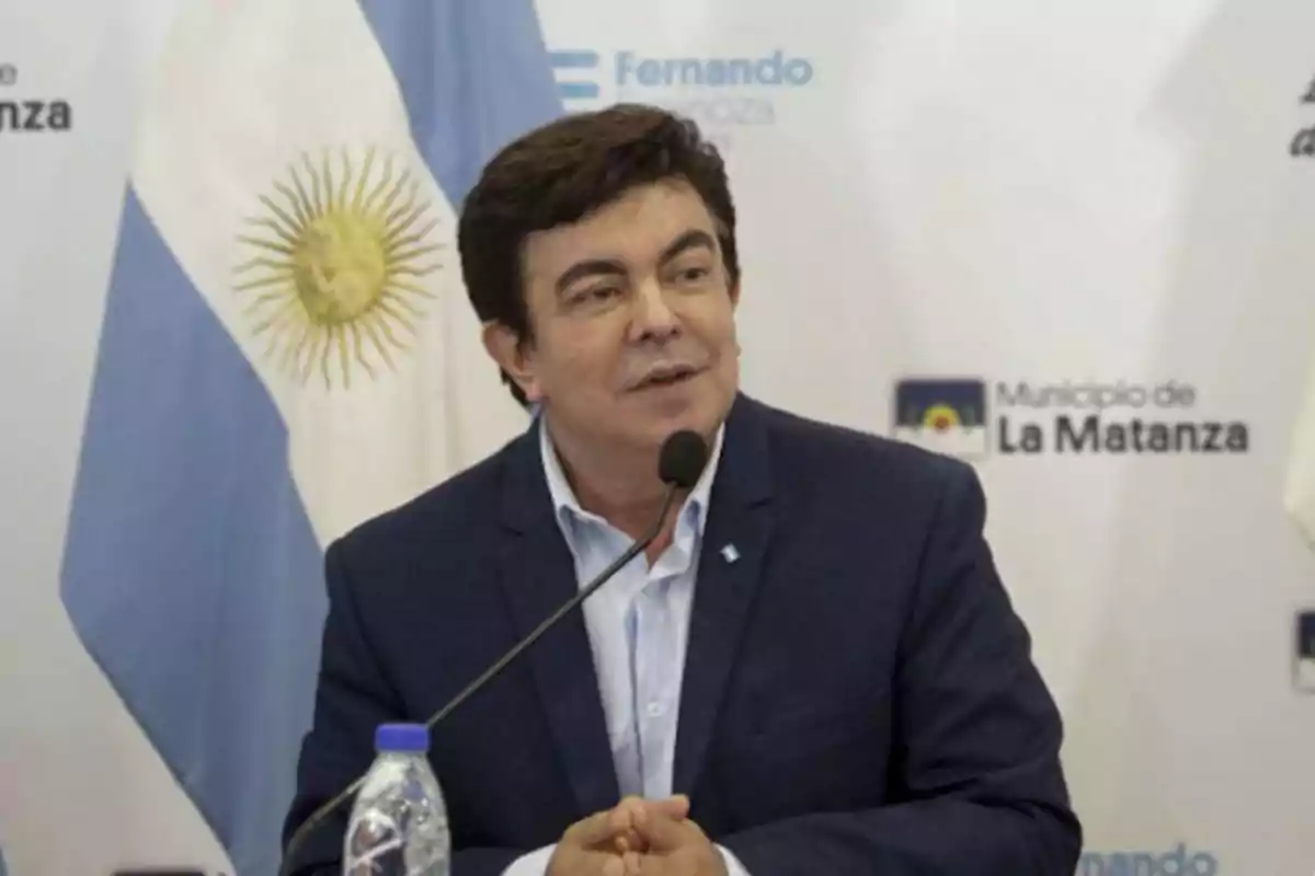 Un hombre hablando en una conferencia con una bandera de Argentina de fondo.