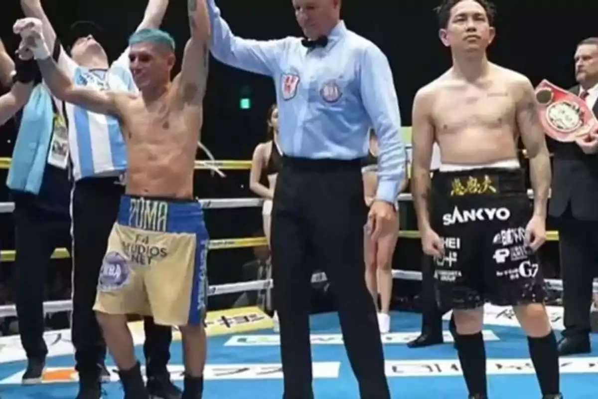Un boxeador con el brazo levantado por el árbitro en señal de victoria mientras otro boxeador observa. Un boxeador con el brazo levantado por el árbitro en señal de victoria mientras otro boxeador observa.