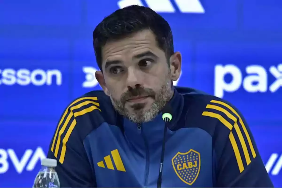 Un hombre con chaqueta deportiva azul y amarilla con el escudo de CABJ en una conferencia de prensa.