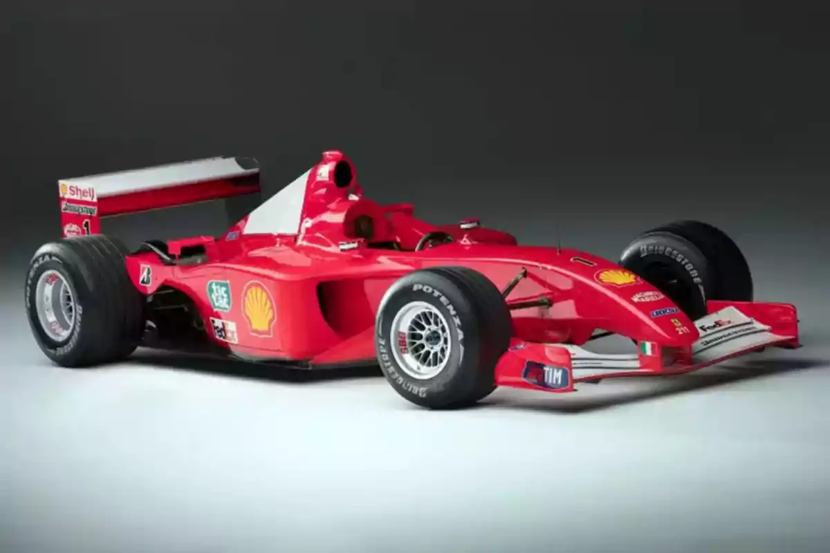 Auto de Fórmula 1 color rojo con logotipos de patrocinadores sobre un fondo gris