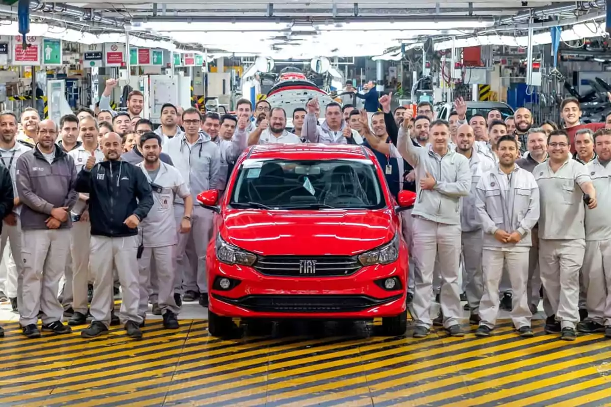 Un grupo de trabajadores de una fábrica de automóviles posando junto a un coche rojo recién ensamblado.