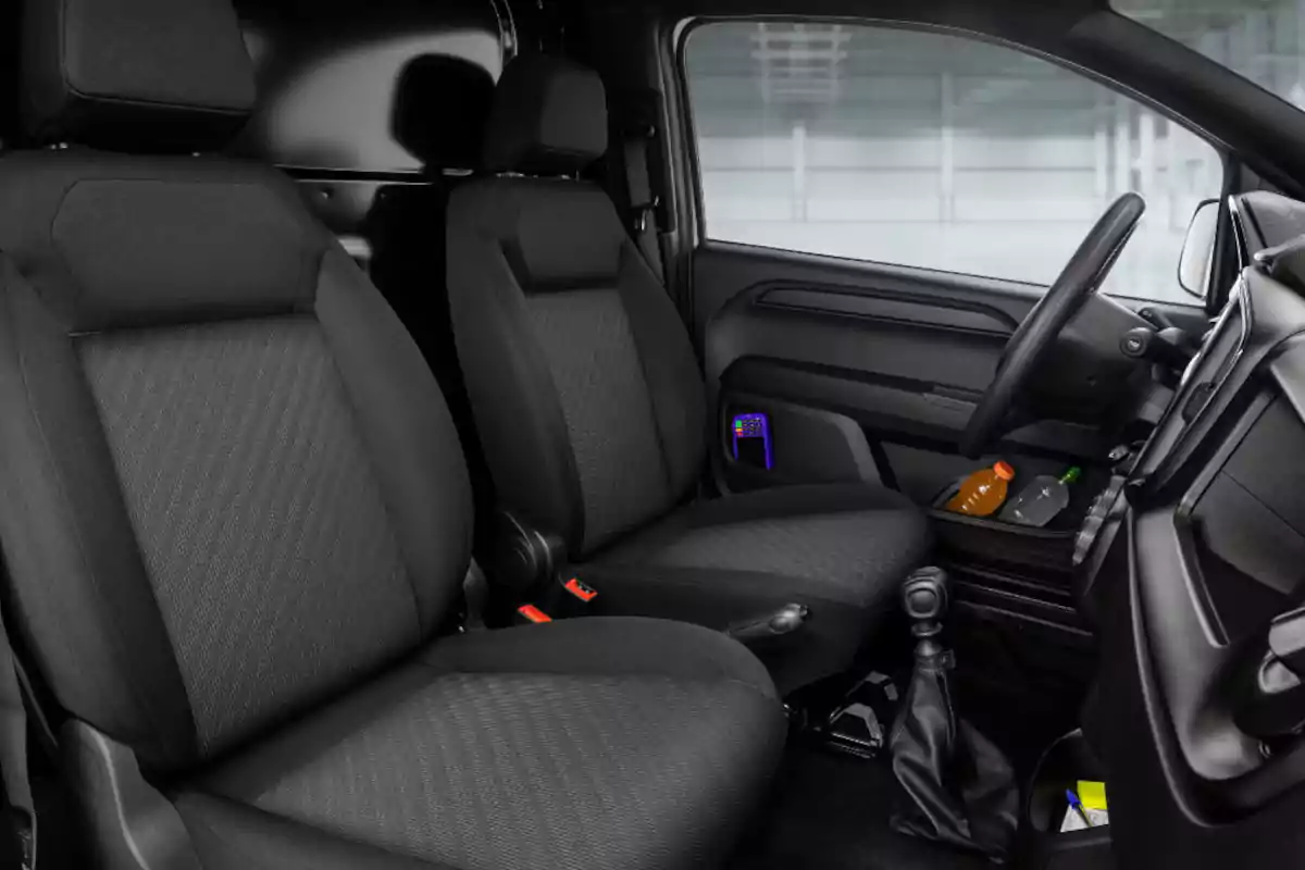 Interior of a vehicle with two black front seats, gear shift, steering wheel, and bottles in the cup holder Interior of a vehicle with two black front seats, gear shift, steering wheel, and bottles in the cup holder