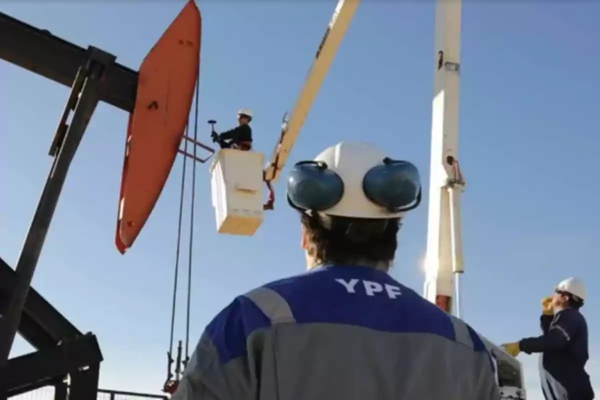 Workers with helmets and safety gear inspect an oil extraction structure under a clear sky.