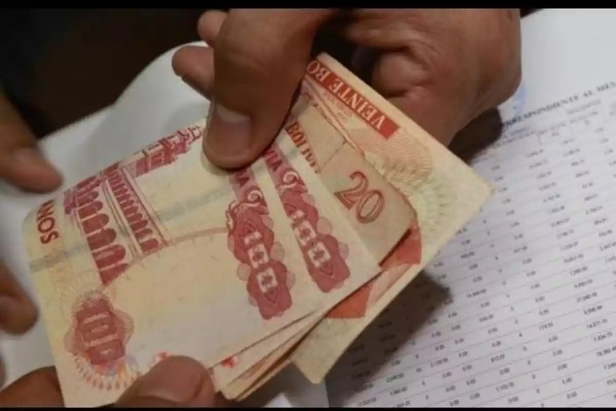 Una persona contando billetes de bolivianos sobre un documento con números. Una persona contando billetes de bolivianos sobre un documento con números.