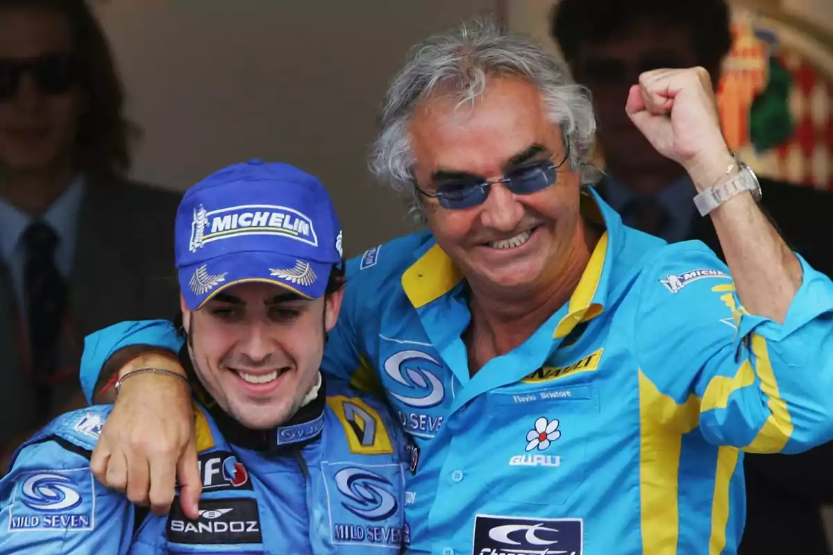 Dos hombres sonríen y celebran juntos vistiendo uniformes azules de un equipo de automovilismo Dos hombres sonríen y celebran juntos vistiendo uniformes azules de un equipo de automovilismo