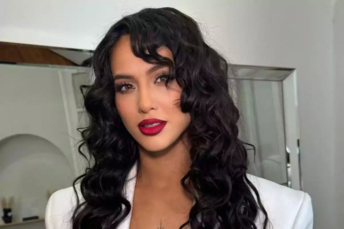 Una persona con cabello rizado oscuro y labios rojos en un entorno interior.