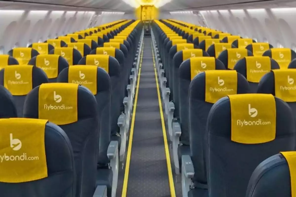 Interior de un avión con filas de asientos azules y reposacabezas amarillos con el logo de Flybondi.