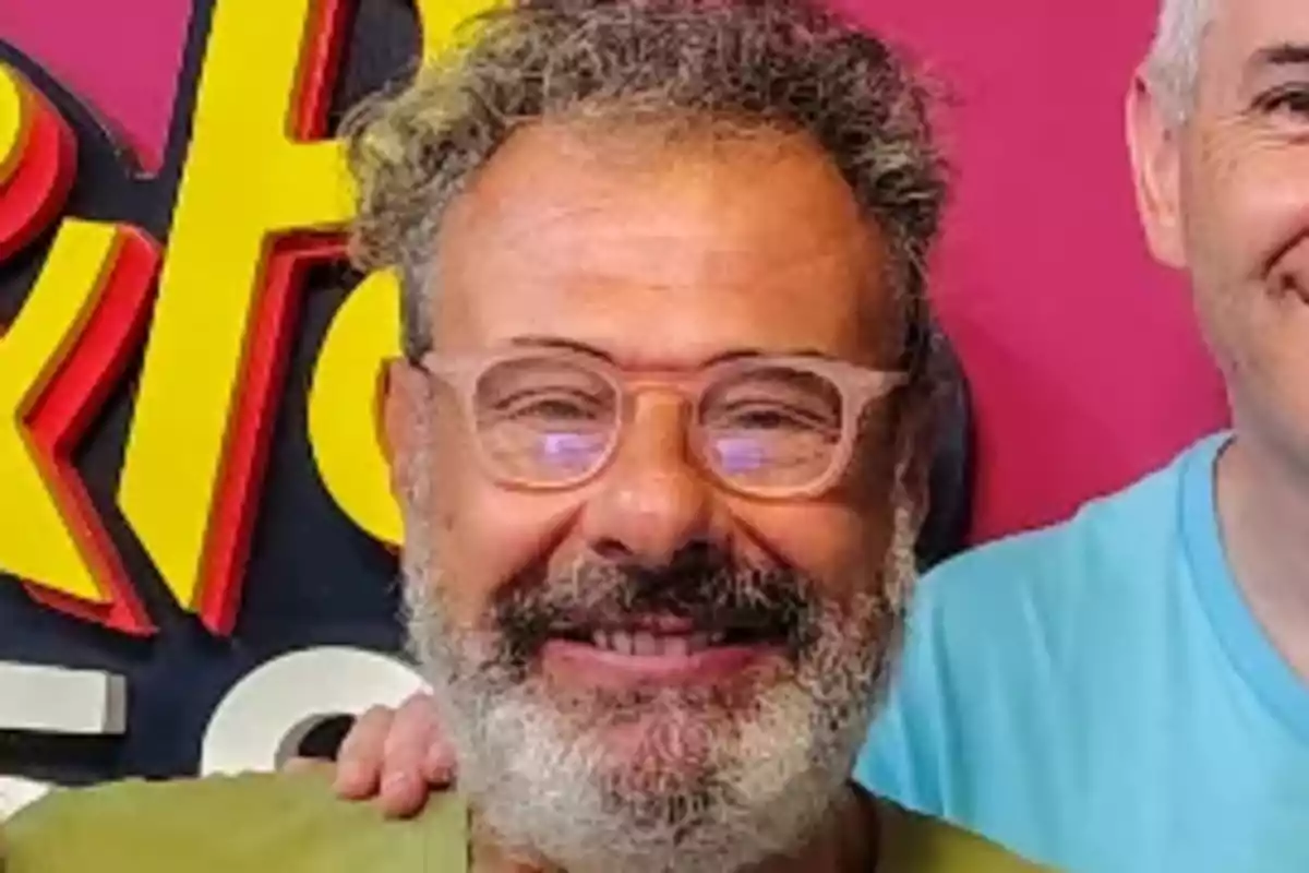 A man with a beard and glasses smiles in front of a colorful background.