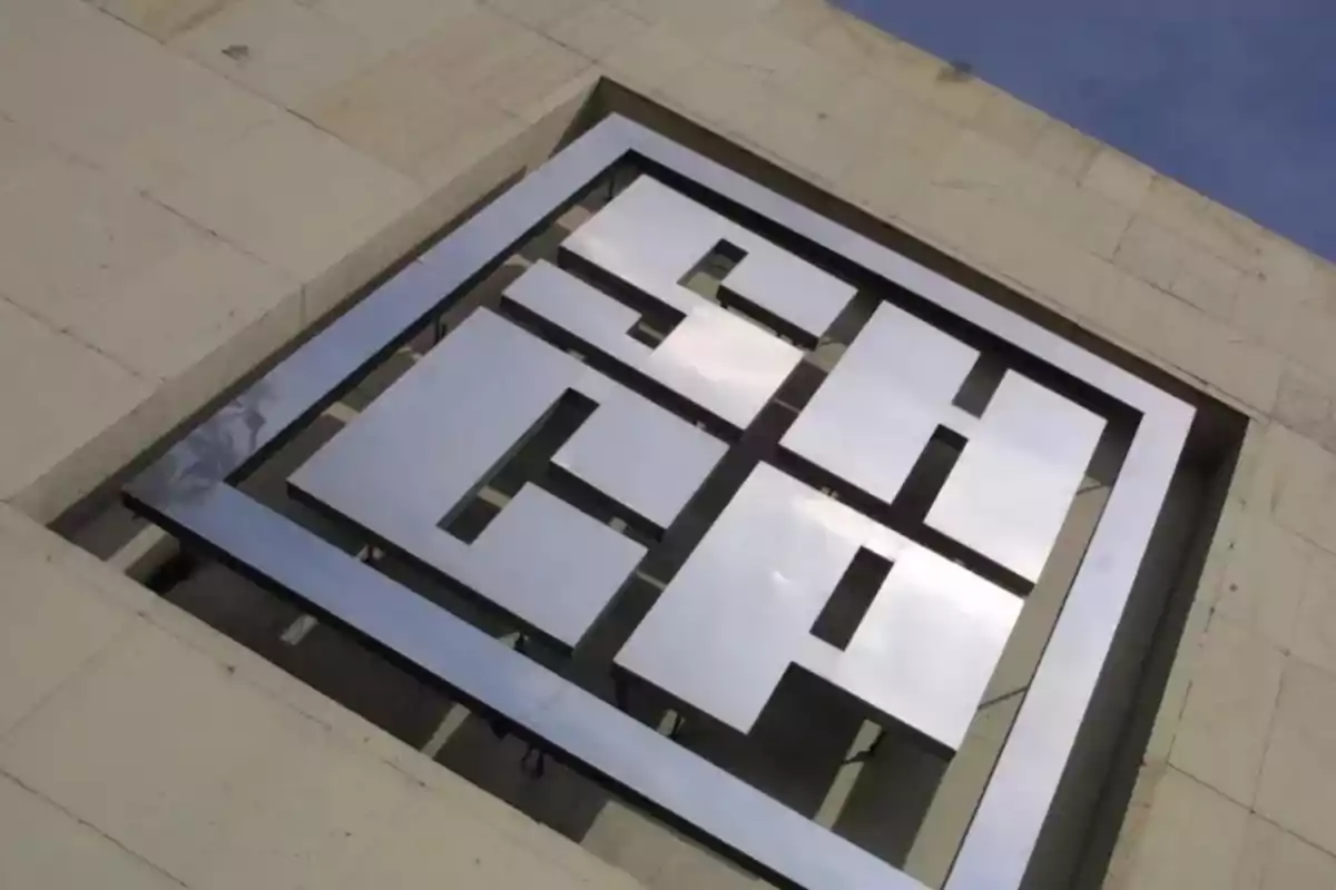 Logotipo metálico en una pared de piedra con cielo azul de fondo.