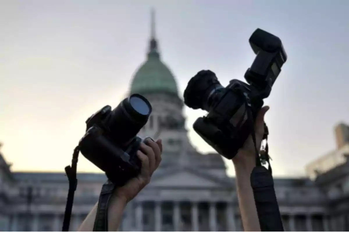 Hands holding cameras in front of a building with a dome at sunset. Hands holding cameras in front of a building with a dome at sunset.
