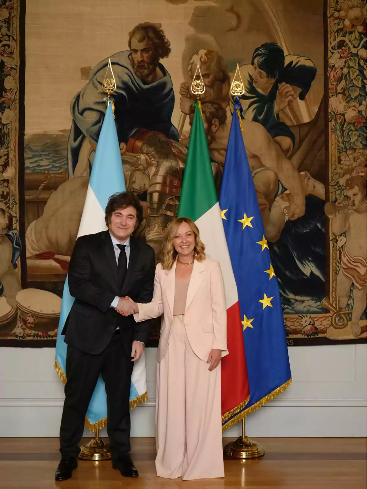 Dos personas dándose la mano frente a las banderas de Argentina, Italia y la Unión Europea, con un tapiz decorativo de fondo Dos personas dándose la mano frente a las banderas de Argentina, Italia y la Unión Europea, con un tapiz decorativo de fondo
